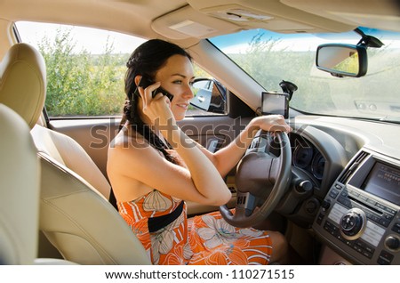 Pretty woman driver sitting behind the steering wheel talking on her mobile phone with the car safely parked at the roadside