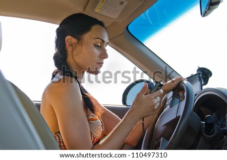 Woman driver sitting behind the steering wheel reading a text message on a mobile