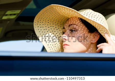 Beautiful woman in a wide brimmed straw hat protecting her eyes from the sunlight sitting in a car