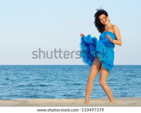 Beautiful woman in a summer dress caught in a windy day at the sea with her skirt and hair blowing up in the breeze