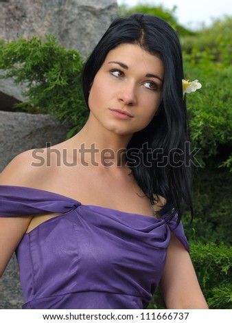 Beautiful woman in an elegant off the shoulder purple dress posing outdoors against a rock