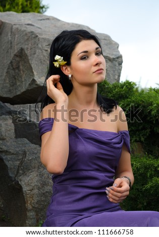 Beautiful glamorous woman posing on a rock in an elegant off the shoulder dress with a flower in her hair