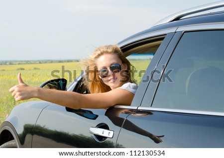Attractive blonde woman leaning out of a car car giving a thumbs up either to show that everything is alright or as a gesture to thumb down a lift