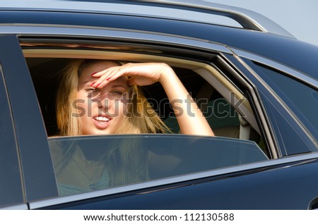 Woman sitting in a motor car peering into the sun through the half open window with her hand shielding her eyes