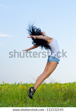 Woman in stilettoes jumping for joy in a graceful curved motion with her arms outspread