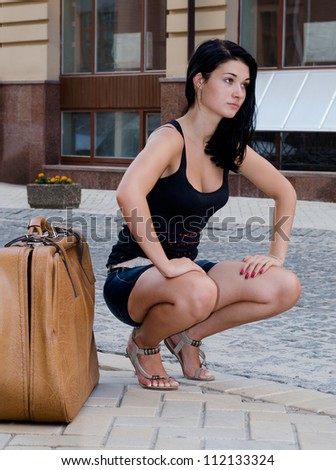 Beautiful woman tourist squatting alongside a large suitcase waiting for a lift