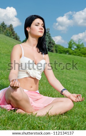 Beautiful girl meditating cross legged on grass with a serene expression and her eyes closed