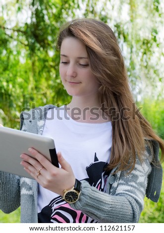 attractive casual young girl working on a touch screen tablet in the park