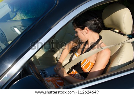 Woman driver obeying traffic rules and tightening her safety belt viewed through the open window of the car