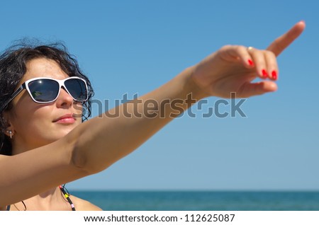 Beautiful woman in sunglasses pointing with an extended arm to the blue sky above her head