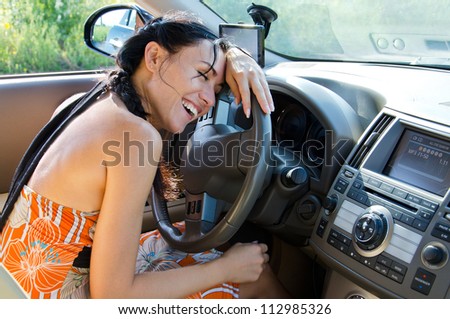 Attractive laughing woman driver leaning on the steering wheel of her car with her eyes shut