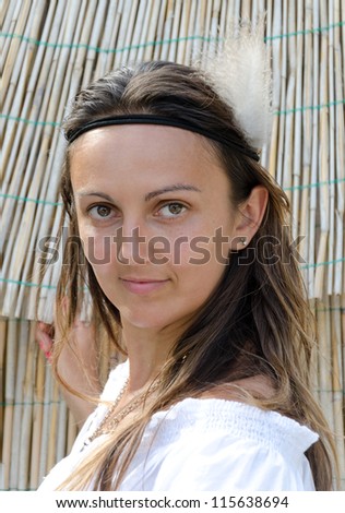 Attractive casual blonde long haired woman wearing a headband in front of a reed hut