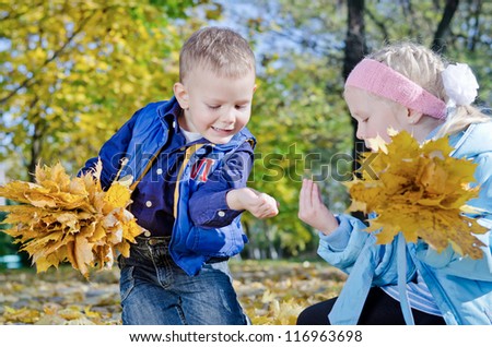 Young children gathering leaves together in outdoor autumn woodland