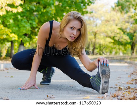 Attractive blonde female athlete warming up with her leg extended as she stretches to reach her toes
