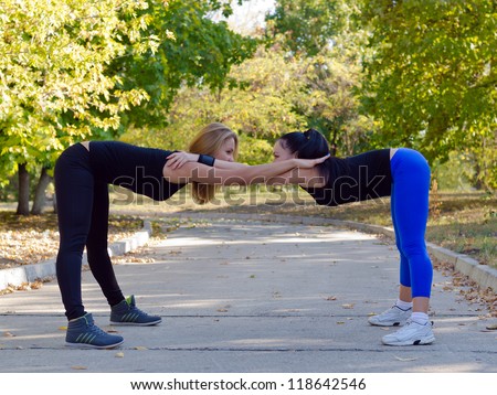 Pair of women working out together doing bending and stretching exercises using each other for mutual support