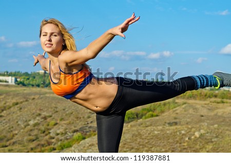 Athletic woman balancing on one leg with her arms outstretched as she works out outdoors in open countryside