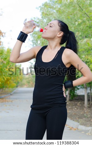 Athletic young woman standing in a rural lane drinking bottled water as she pauses for a break in her work out