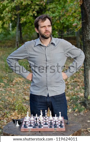 Young man contemplating his next chess move standing outdoors with hands on hips