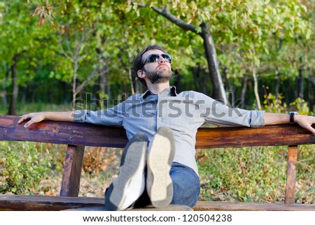 Young man relaxing on a park bench with his feet up and head thrown back looking at the sun