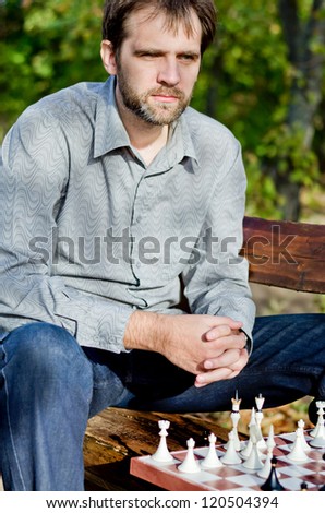 Man sitting outdoors on a wooden bench thinking deeply about his chess game as he considers his next move