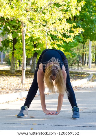 Woman limbering up for exercises bending down towards the ground with her hands clasped to stretch her muscles