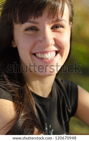 Closeup cropped portrait of a vivacious young woman laughing at the camera while sitting in evening sunshine