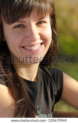 Charming young brunette woman with a beautiful smile looking into the camera in evening sunlight