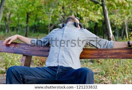 Exhausted man relaxing on a bench in woodland with his head thrown back and his arms outspread along the top of the bench