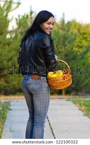 Smiling woman carrying a basket of apples looking back over her shoulder at the camera with a lovely smile as she walks away down a path