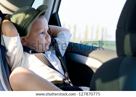 Little boy in a child safety seat sitting patiently in the back of a car with his hands behind his head staring out of the window