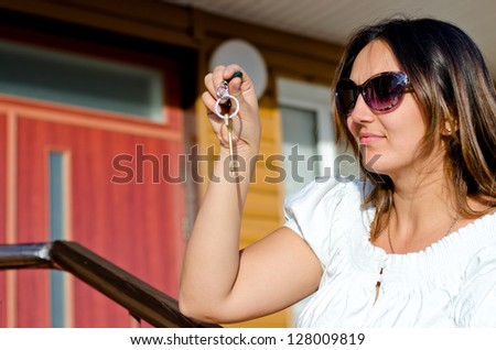 Smiling woman wearing sunglasses holding up the key to a property dangling from her hand conceptual of ownership or rental of a residence or vacation house