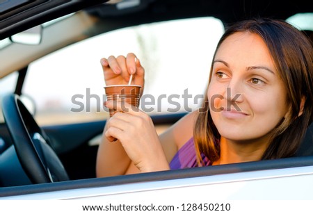 Attractive young woman sitting in the drivers seat of her car enjoying a takeaway cup of coffee in a disposable mug