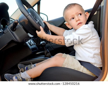 Cute little boy pretending to drive strapped in securely to the drivers seat of a car with his hands on the wheel
