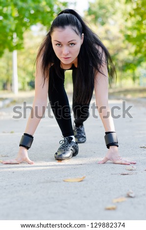 Woman athlete in the starting position for a run crouched down on a rural road facing the camera in a park as she starts her training