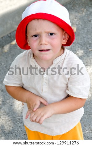 Cute little boy in a summer outfit and sun hat with a puzzled expression frowning as he looks up at the camera in uncertainty