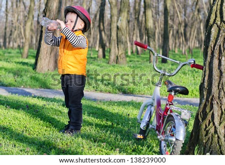 Thirsty little boy out riding his bicycle along a path through rural woodland stopping to drink bottled water