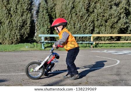 Little boy playing with his bike outdoors dressed in a colourful safety helmet and high visibility jacket preparing to go for a ride