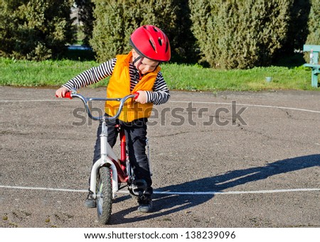 Cute little boy out riding his bike dressed in colourful safety gear stopping to check something, standing astride the bike looking at the ground