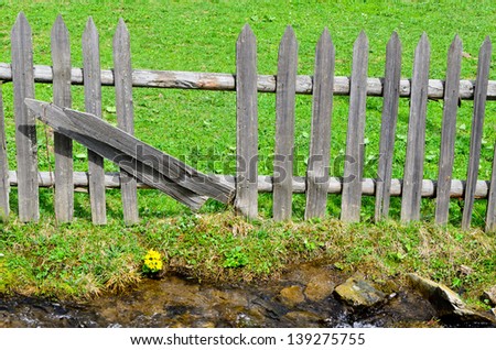 Line of weathered rustic wooden palisade fencing with two uprights turned sideways to make a partial opening