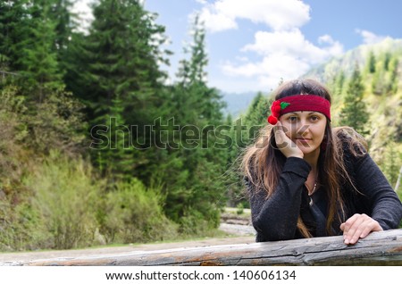 Pretty woman wearing a colourful headband in a forested valley relaxing looking at the camera with her chin resting on her hand