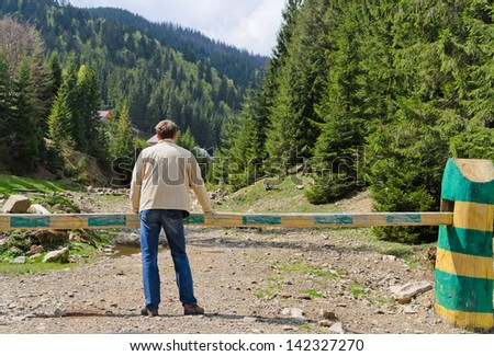 Man standing with his back to the camera admiring a forested valley with steep mountain slopes