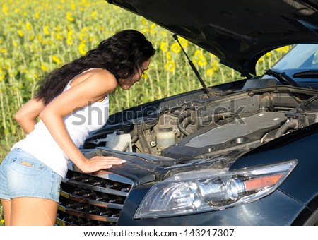 Woman leaning over looking into the engine compartment of a broken down car