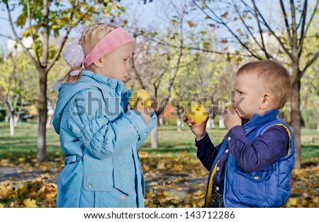 Cute little blonde brother and sister eating fresh apples in the park while enjoying an autumn day outdoors