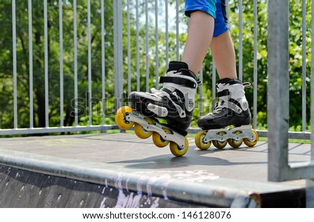 Closeup of the feet of a young girl wearing rollerblades standing on top of a ramp at a skate park while out roller skating