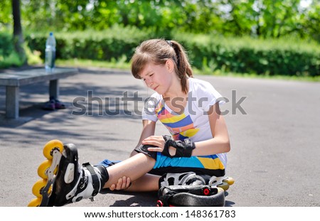 Young attractive teenage skater grimacing in pain and nursing her injured knee and leg after taking a fall on the asphalt at the skating rink