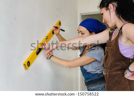Two young female decorators working as a team measuring and marking the wall with a spirit level