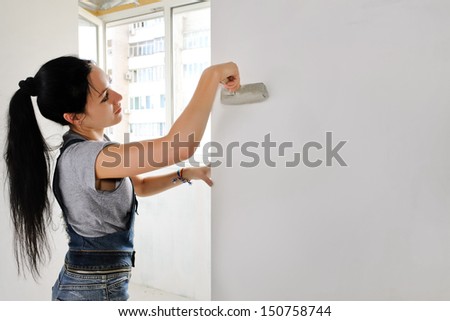 Woman painting an apartment wall finishing off the redecorating with a paintbrush