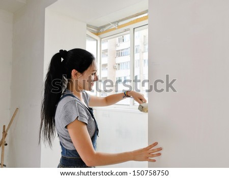 Woman painting a wall of an apartment with a paintbrush carefully finishing off around a window frame