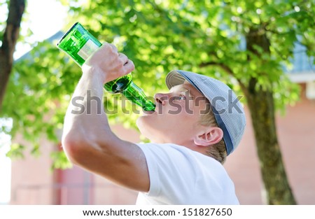 Alcoholic standing outdoors drinking directly from the bottle of spirits with his head tilted back gulping down the contents