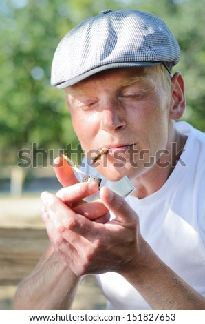 Close up of the face and hands of a man lighting up a homemade cigarette rolled from loose ground tobacco outdoors in a park